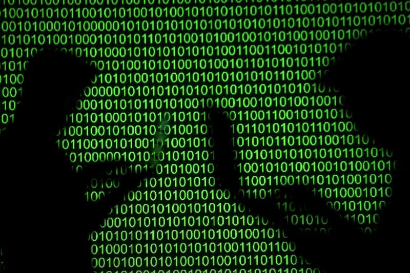 Silhouettes of laptop users are seen next to a screen projection of binary code are seen in this picture illustration