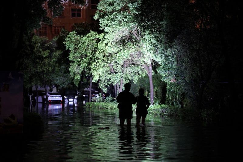 Residents use flashlights as they wade through floodwaters inside a residential compound, following heavy rainfall brought by remnants of Typhoon Dolphin, in Pingdingshan