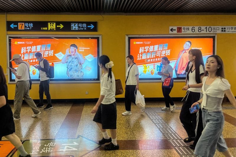 People walk past billboards from Innovent Biologics and Meituan displayed in a metro station in Shanghai
