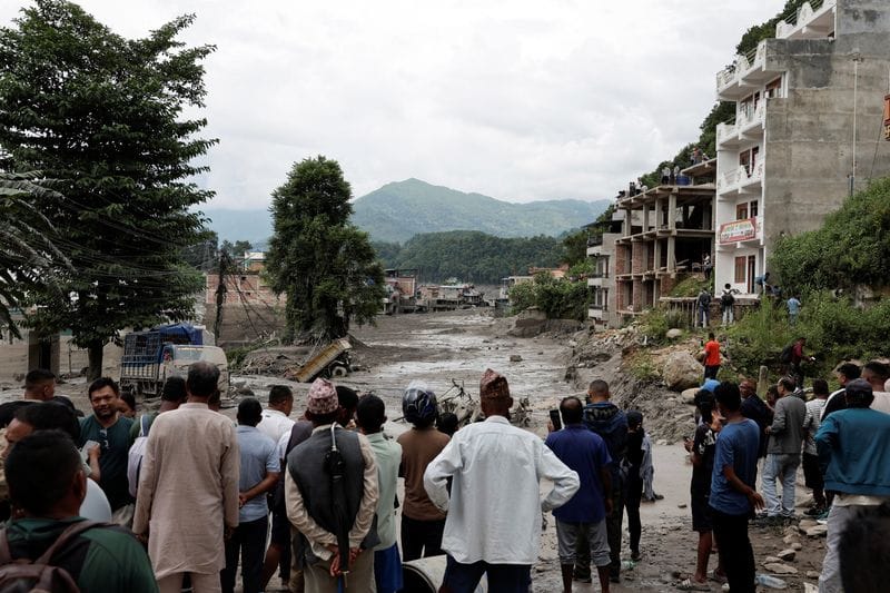 People stand near mud covered houses and a road, following a flash flood at Trishuli, Nepal