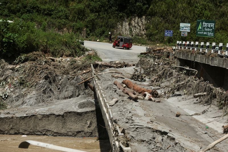 An auto rickshaw drives past a broken bridge following a flash flood in Galchhi