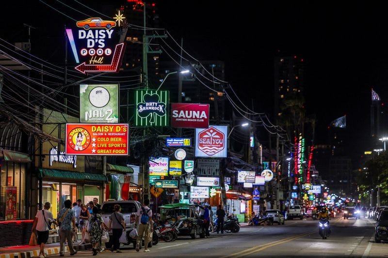 People walk along a street lined with bars and entertainment venues at Jomtien Beach, in Pattaya