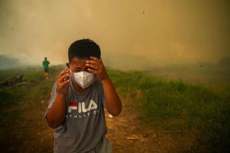 A boy reacts as smoke rises from wildfires at a residential area in Ogan Ilir, South Sumatra province