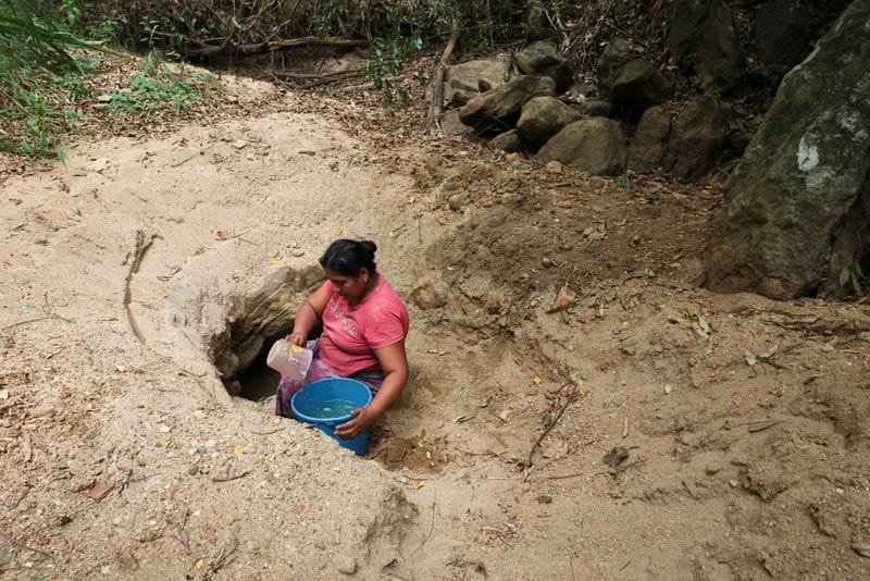 A woman draws water from a hole dug in a dry riverbed using a mug in Monaragala district
