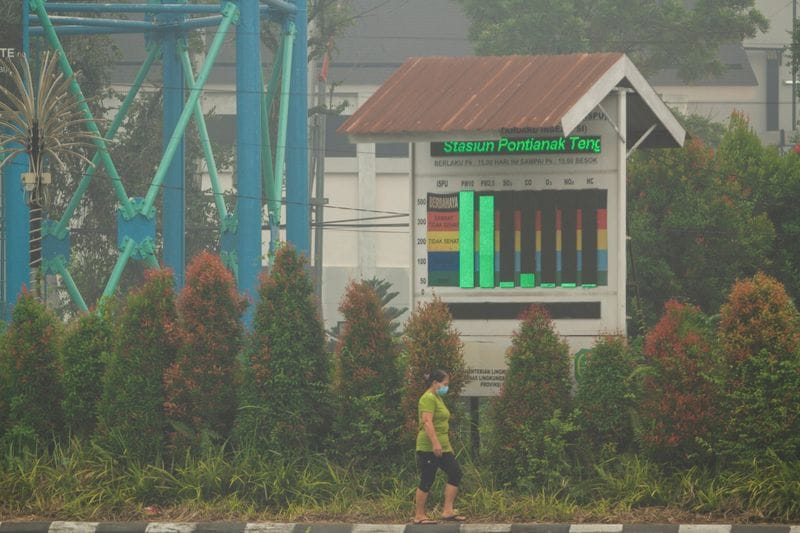 A woman wearing a protective face mask walks past near an air quality display while haze from wildfires covers the area in Pontianak