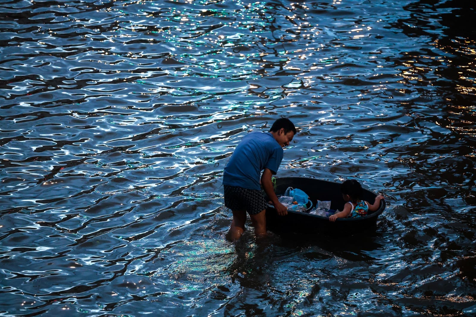 A father pulls a plastic basin carrying his son and groceries as he wades through a flooded area following heavy rain in Bangkok, Thailand, September 28, 2026. REUTERS/Patipat Janthong
