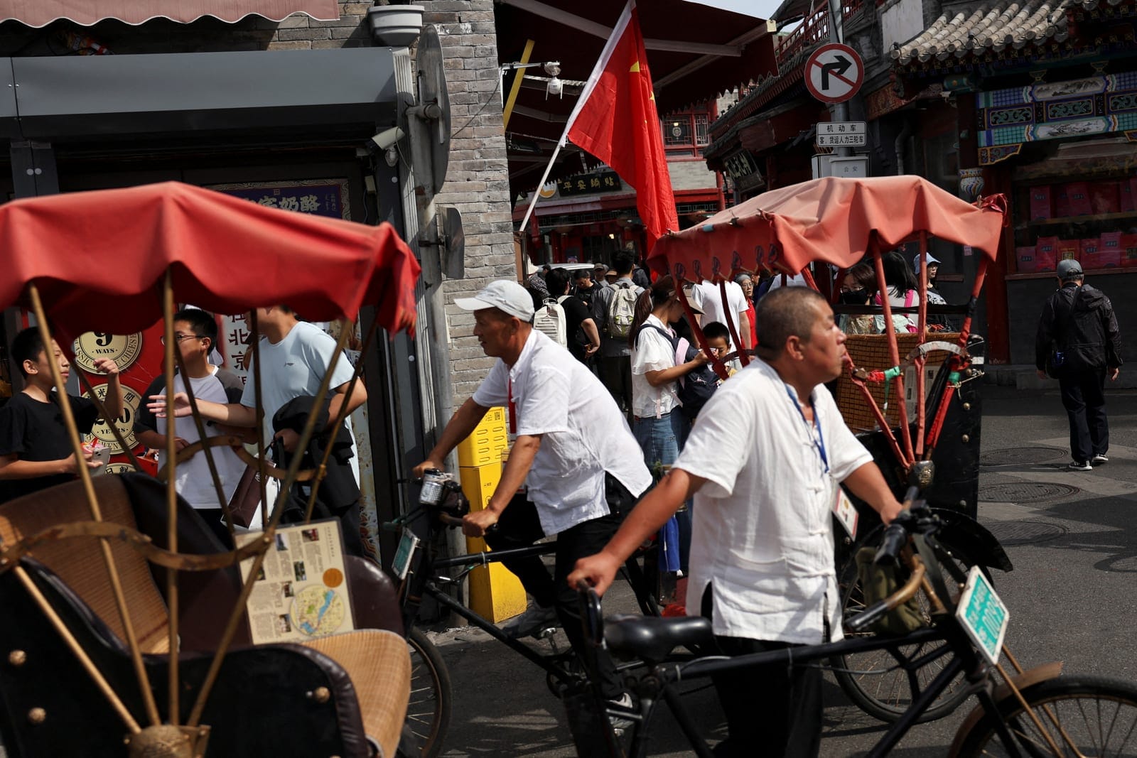 FILE PHOTO: Rickshaw drivers pass a shop decorated with a Chinese flag in the Shichahai area on National Day, the first day of China's eight-day Golden Week holiday, in Beijing, China October 1, 2025. REUTERS/Florence Lo/File Photo