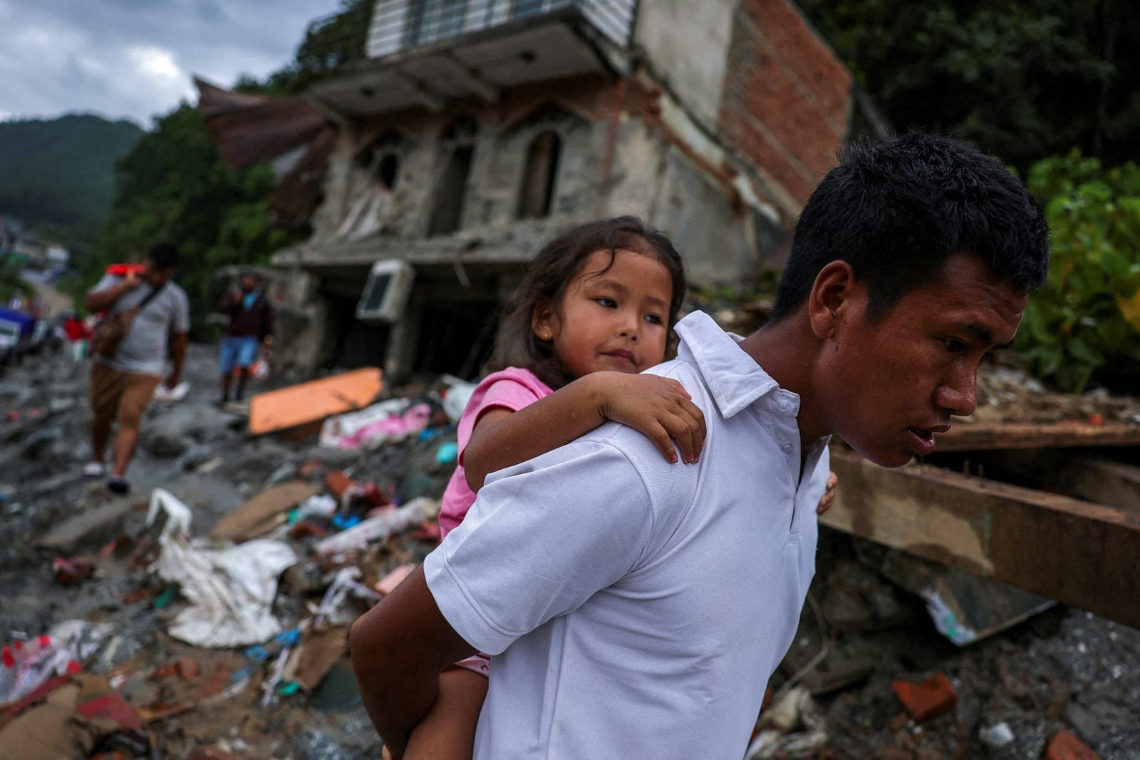 A man carries a girl next to damaged buildings following the deadly flash floods and mudslides in Nuwakot district, Nepal, September 3, 2026. REUTERS/Athit Perawongmetha