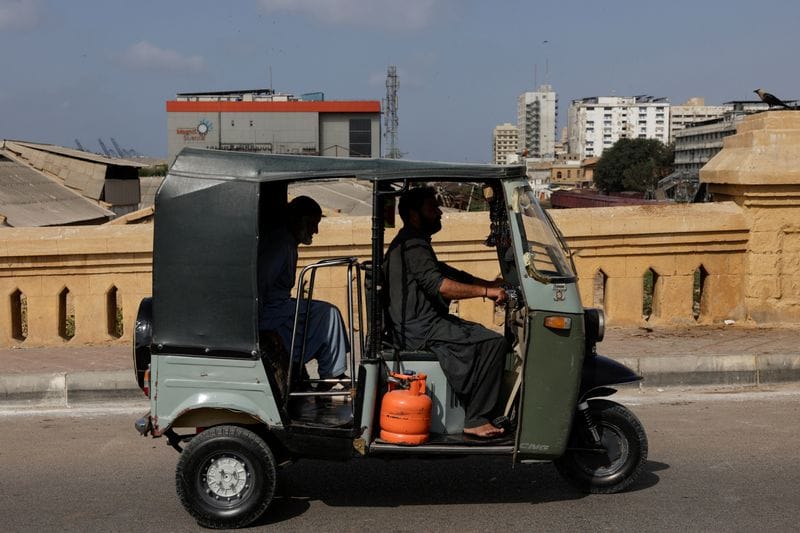A motorised auto-rickshaw powered by liquefied petroleum gas (LPG) passes a bridge amid rising fuel and LPG prices due to the Iran conflict, in Karachi
