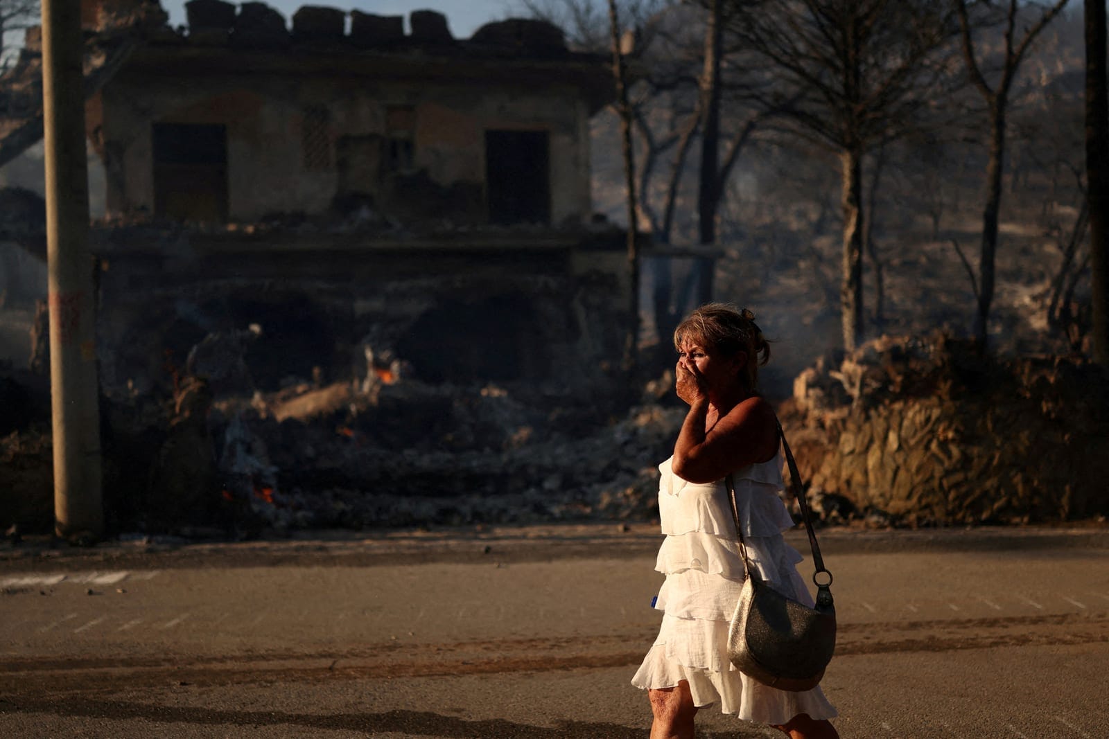 FILE PHOTO: A woman reacts as she walks near a burnt house during a wildfire in Peristeria area, Salamina island, near Athens, Greece, August 16, 2026. REUTERS/Stelios Misinas/File Photo