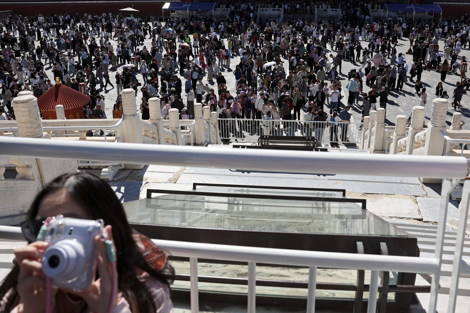 A woman holds a camera as visitors tour the Temple of Heaven, also known as Tiantan Park, on National Day, the first day of China's Golden Week holiday, in Beijing, China, October 1, 2026. REUTERS/Florence Lo
