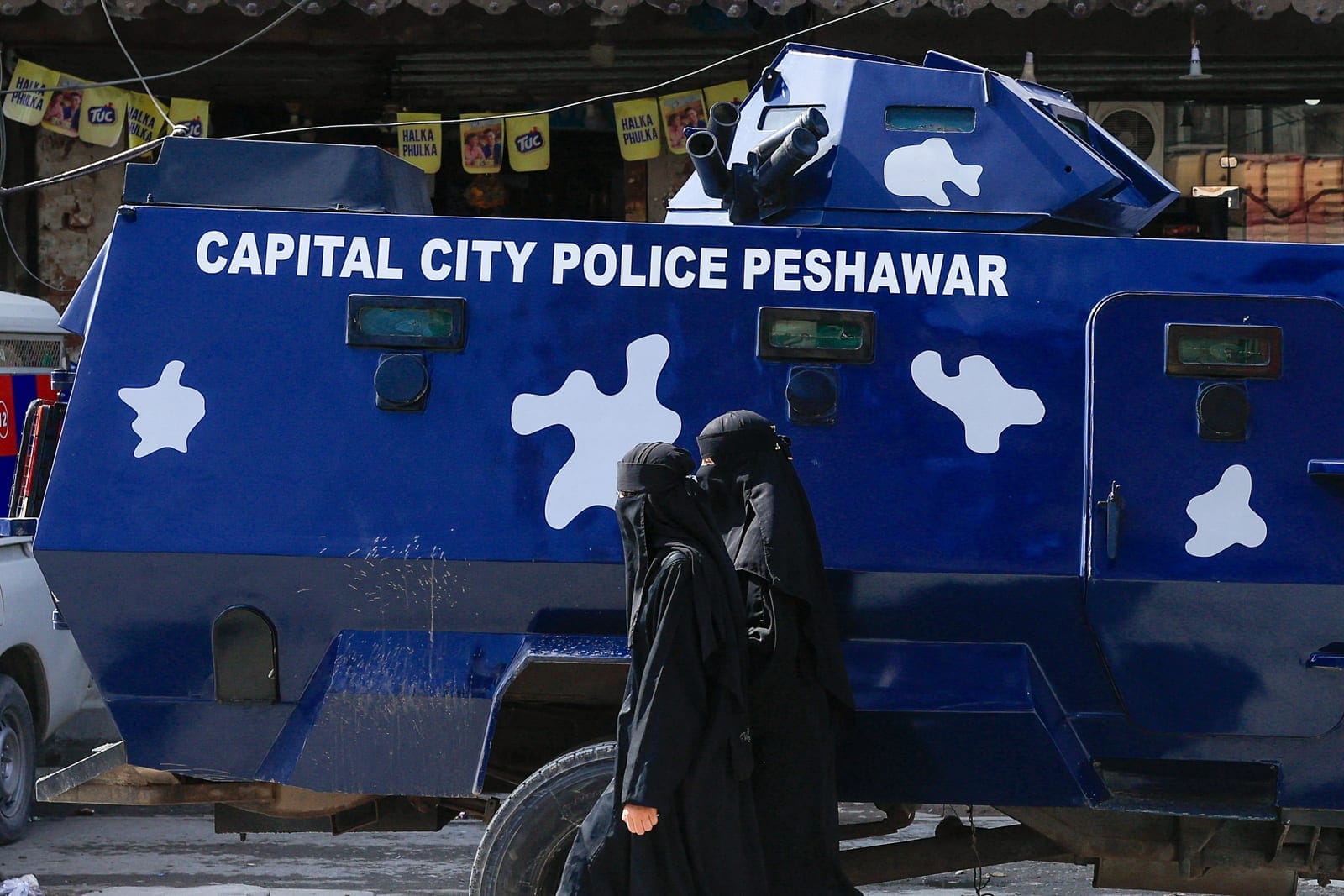 Women wearing burqas walk past a police armoured personnel carrier (APC) deployed as a security measure following a protest call by supporters of jailed former Pakistani Prime Minister Imran Khan's party, Pakistan Tehreek-e-Insaf (PTI), a day after P