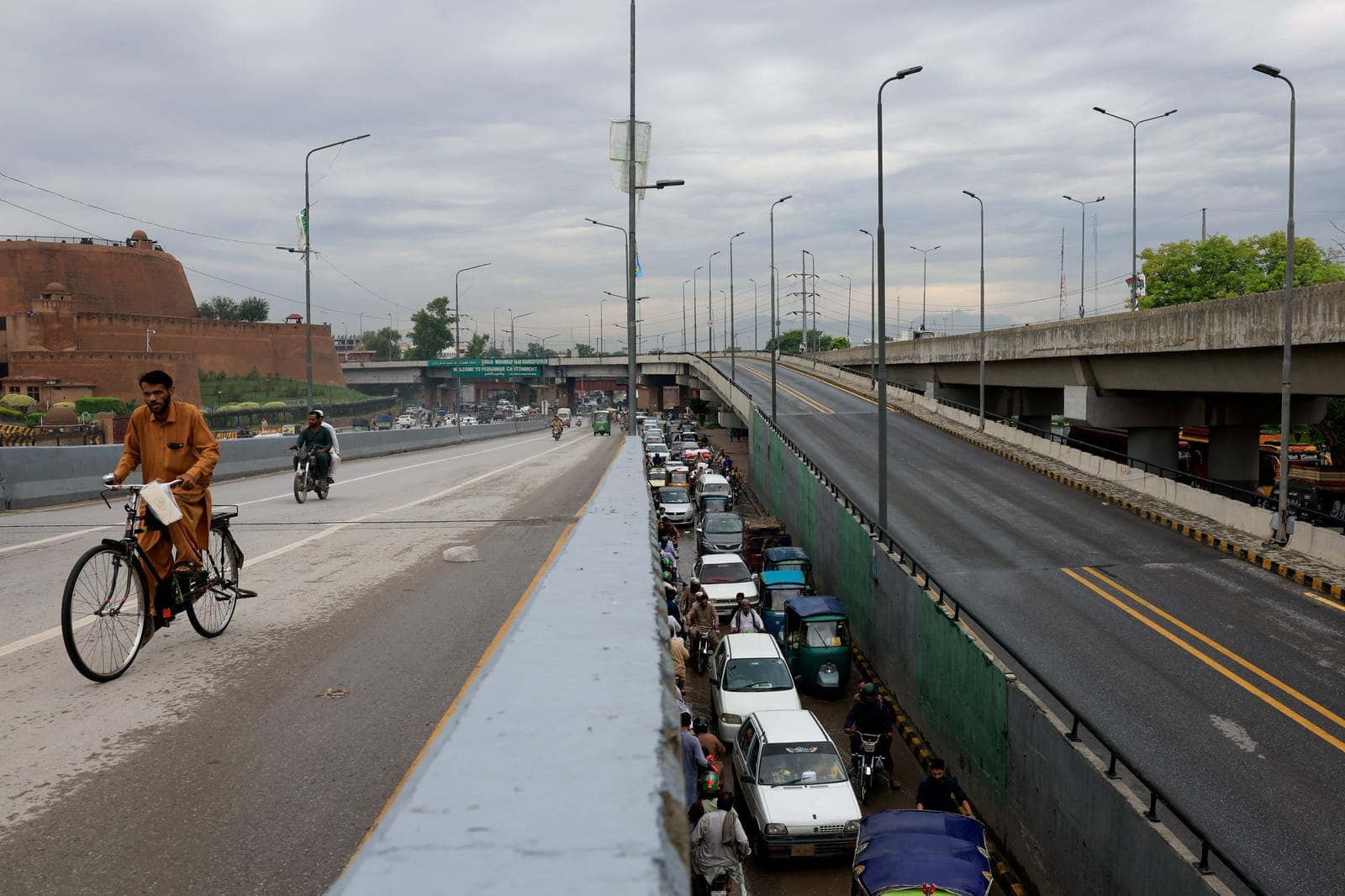 A man rides a bicycle as traffic moves under a bridge, days after Pakistan imposed a state of emergency in Khyber Pakhtunkhwa province and suspended the provincial government led by the party of jailed former Prime Minister Imran Khan, in Peshawar, P