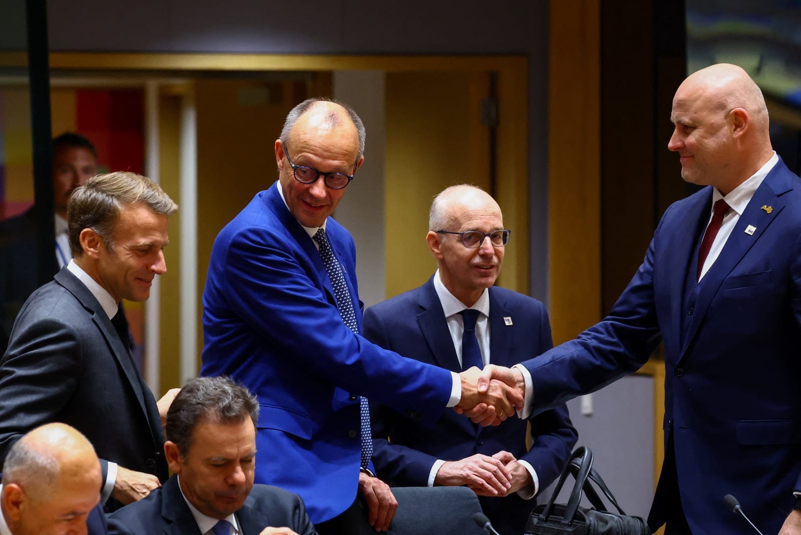 French President Emmanuel Macron reacts as German Chancellor Friedrich Merz and Prime Minister of Latvia Andris Kulbergs shake hands, on the day of the European Union leaders' summit in Brussels, Belgium October 15, 2026. REUTERS/Yves Herman