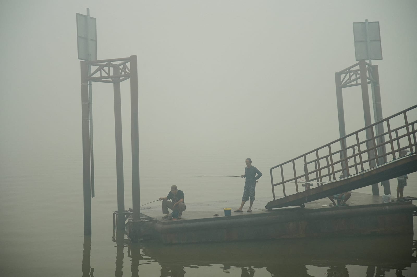 People fish on the Musi River as haze from wildfires shrouds the area in Palembang, South Sumatra province, Indonesia, October 15, 2026. REUTERS/Abriansyah Liberto