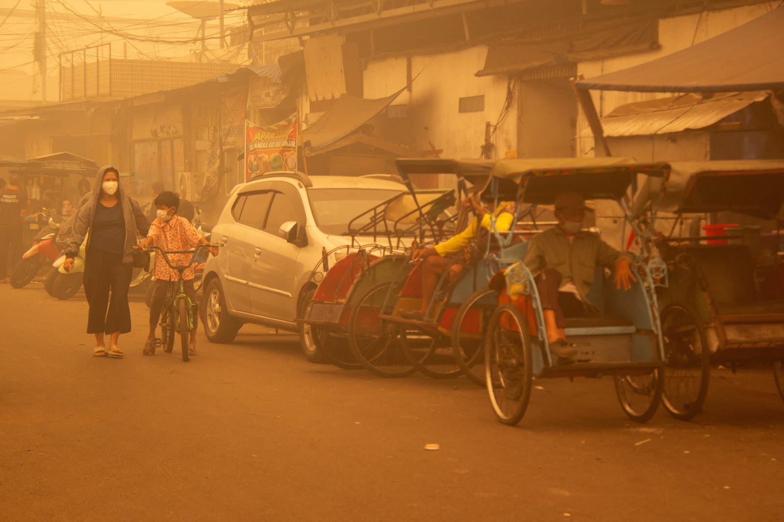 People wearing protective masks walk through the street as haze from wildfires shrouds the area in Palangka Raya, Central Kalimantan province, Indonesia, October 14, 2026. REUTERS/Arief Rahman Septian Prathama