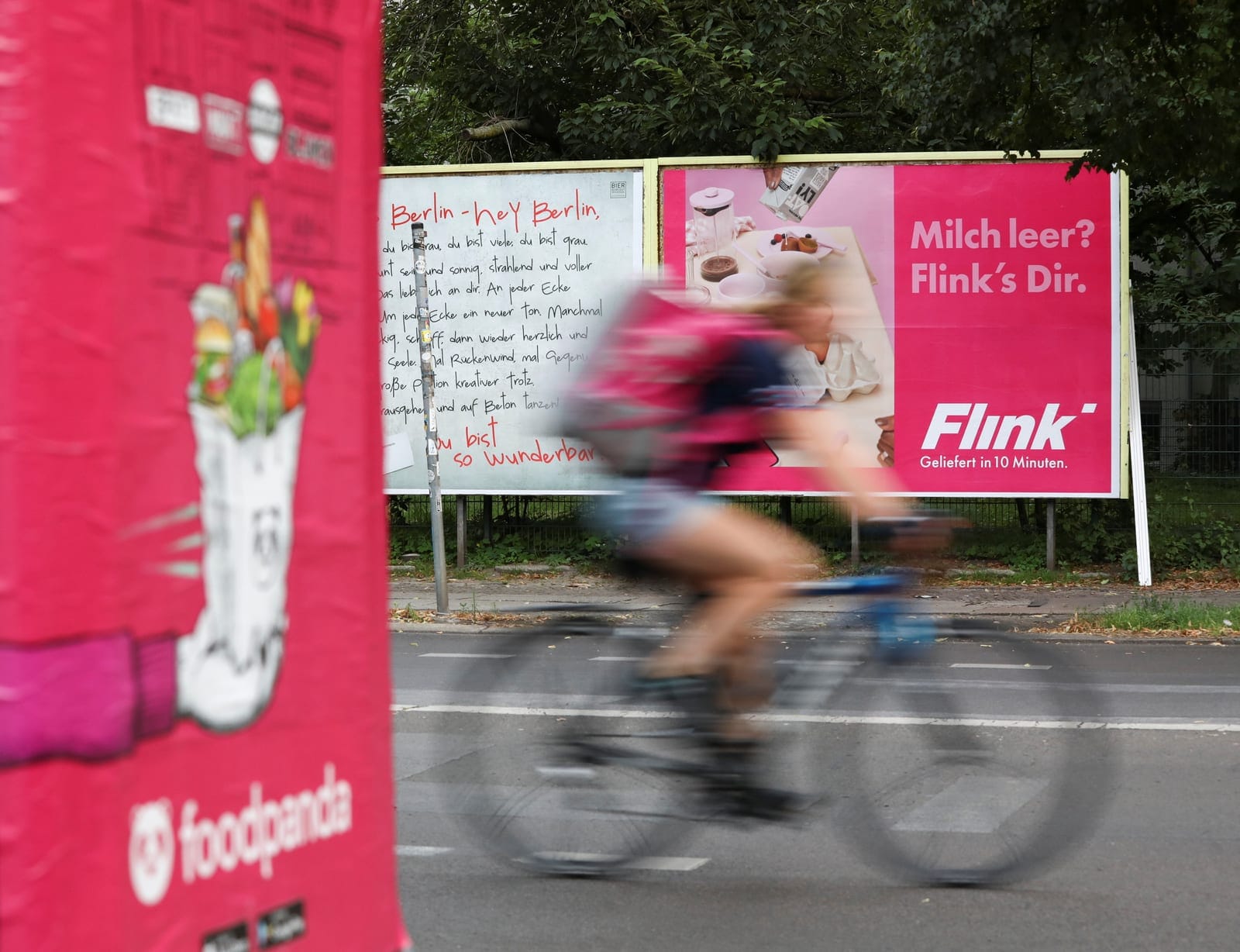 A bicycle courier drives past two advertisements promoting the grocery delivery companies "Flink" and "foodpanda", in Berlin, Germany, August 13, 2021. Picture taken August 13, 2021. REUTERS/Christian Mang