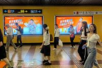 People walk past billboards from Innovent Biologics and Meituan displayed in a metro station in Shanghai