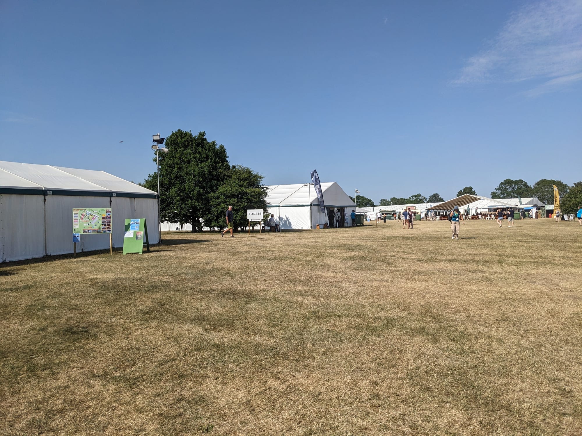 Large marquees stand in a parched field under a blue sky