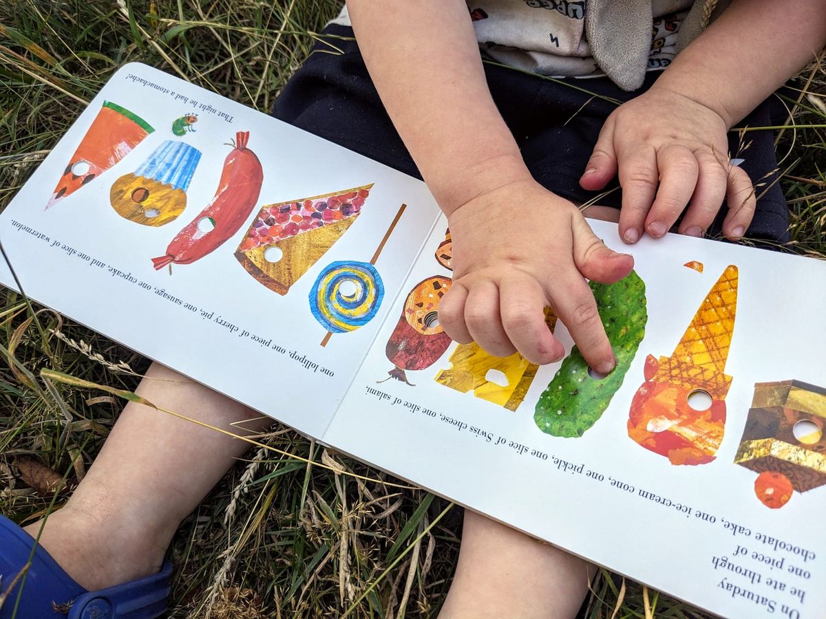 A toddler pokes a finger through a hole in the page of The Very Hungry Caterpillar