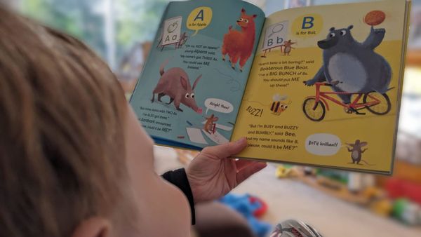 A young boy reads the Usborne Rhyming Alphabet book with illustrations of an aardvark and a blue bear
