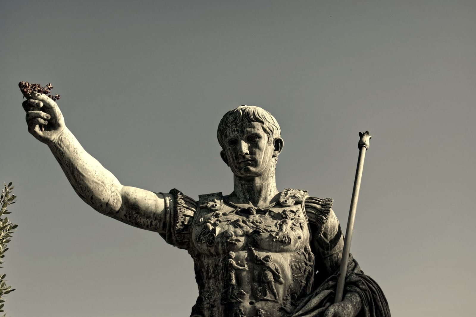Estatua de bronce de un emperador romano con armadura, fotografiada en blanco y negro entre columnas de travertino.