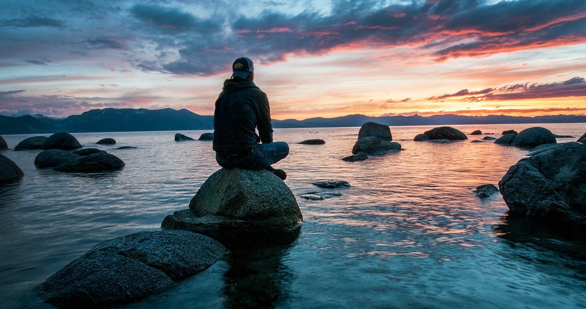 person sitting on rock surrounded by water