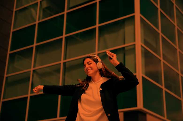 Young woman dancing with headphones in front of commercial building.