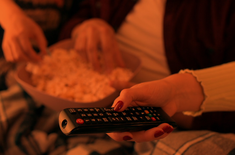 Woman holding a remote control and popcorn.