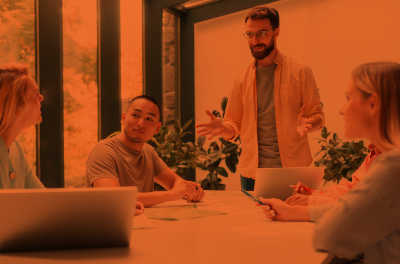 Meeting of a diverse team with a young professional standing and speaking.