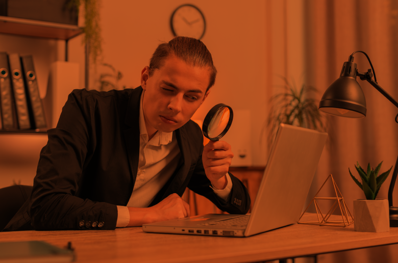 Guy holding a zooming glass over a laptop. 
