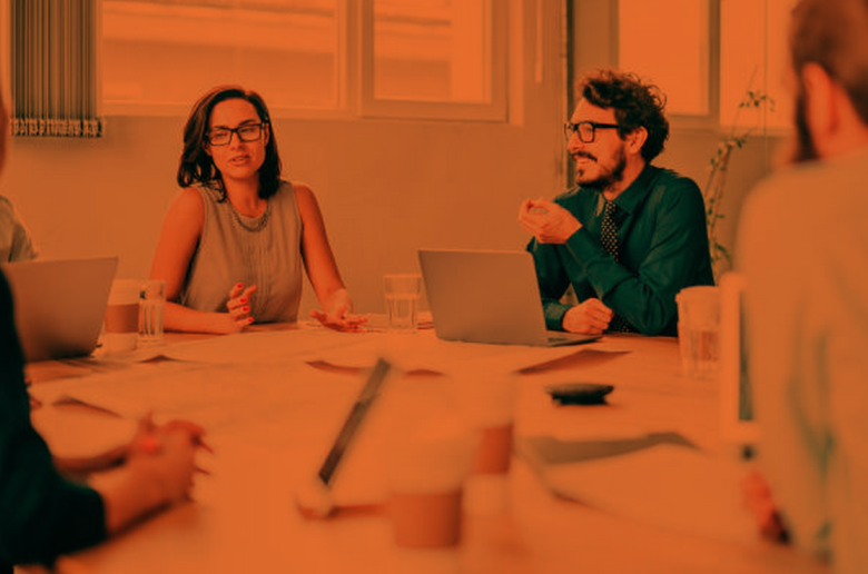 Team having a meeting a young man speaking and a young woman chatting.