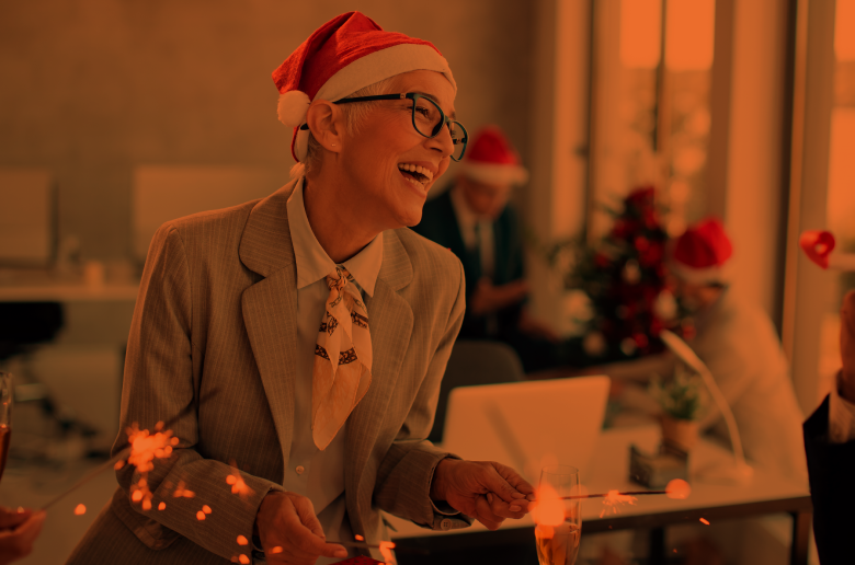 Professional woman celebrating Christmas at work wearing a Santa hat and laughing. 