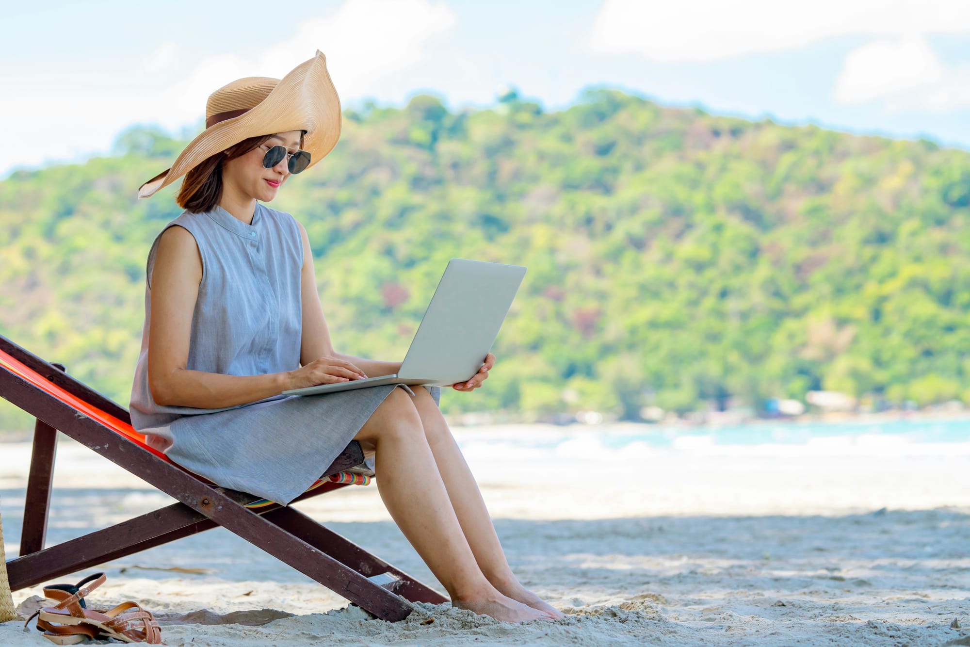 Woman working on a laptop from a beach chair, preparing for the September hiring surge.