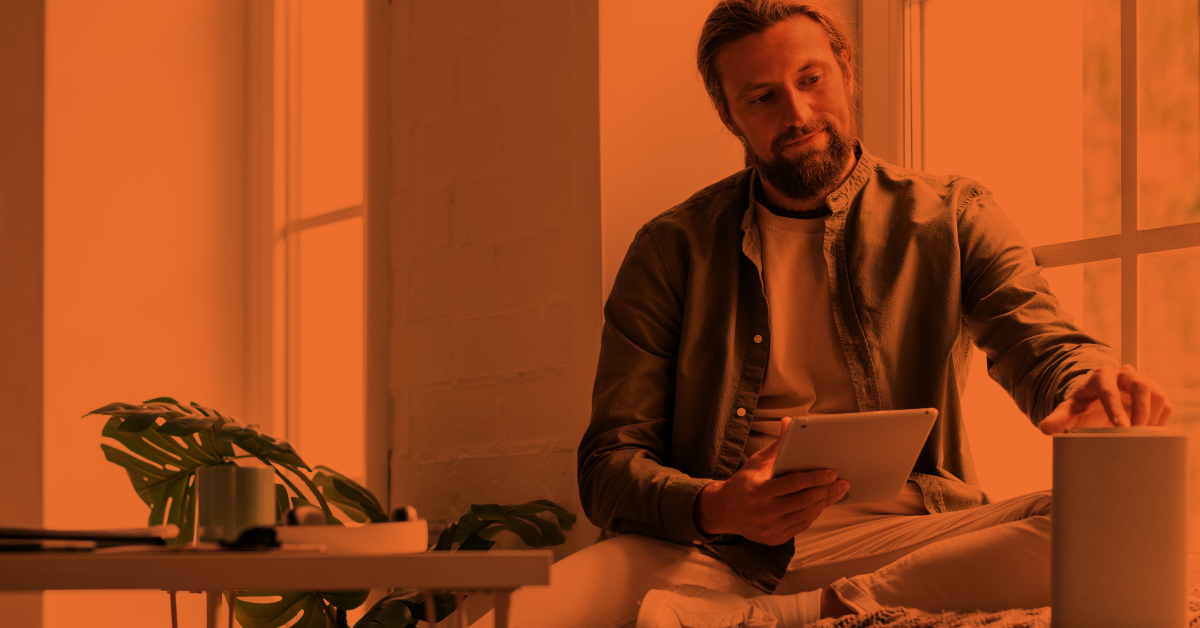 Young man sitting and holding a tablet while turning on a music speaker. 
