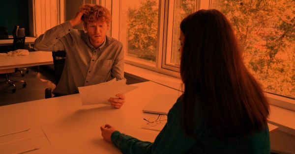 A guy sitting with a recruiter during an interview looking anxious. 
