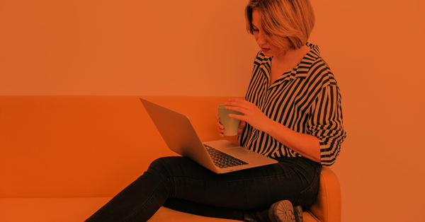 Professional job seeker sitting on a couch holding a laptop and cup of coffee. 