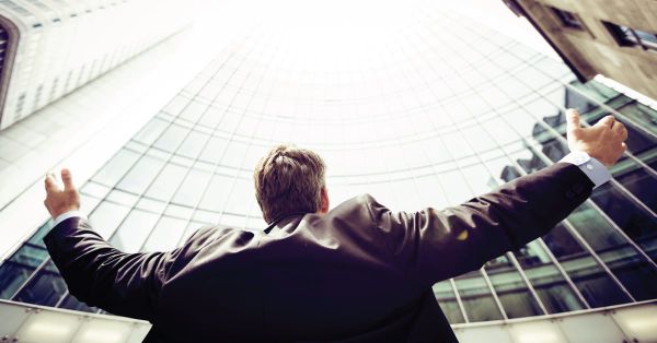 Professional man looking at a business tower and raising his arms. 
