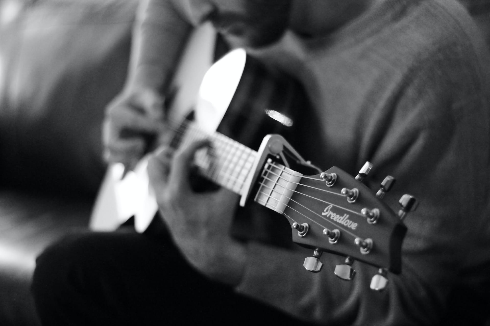 Person playing an acoustic guitar which is fitted with a capo on fret 3