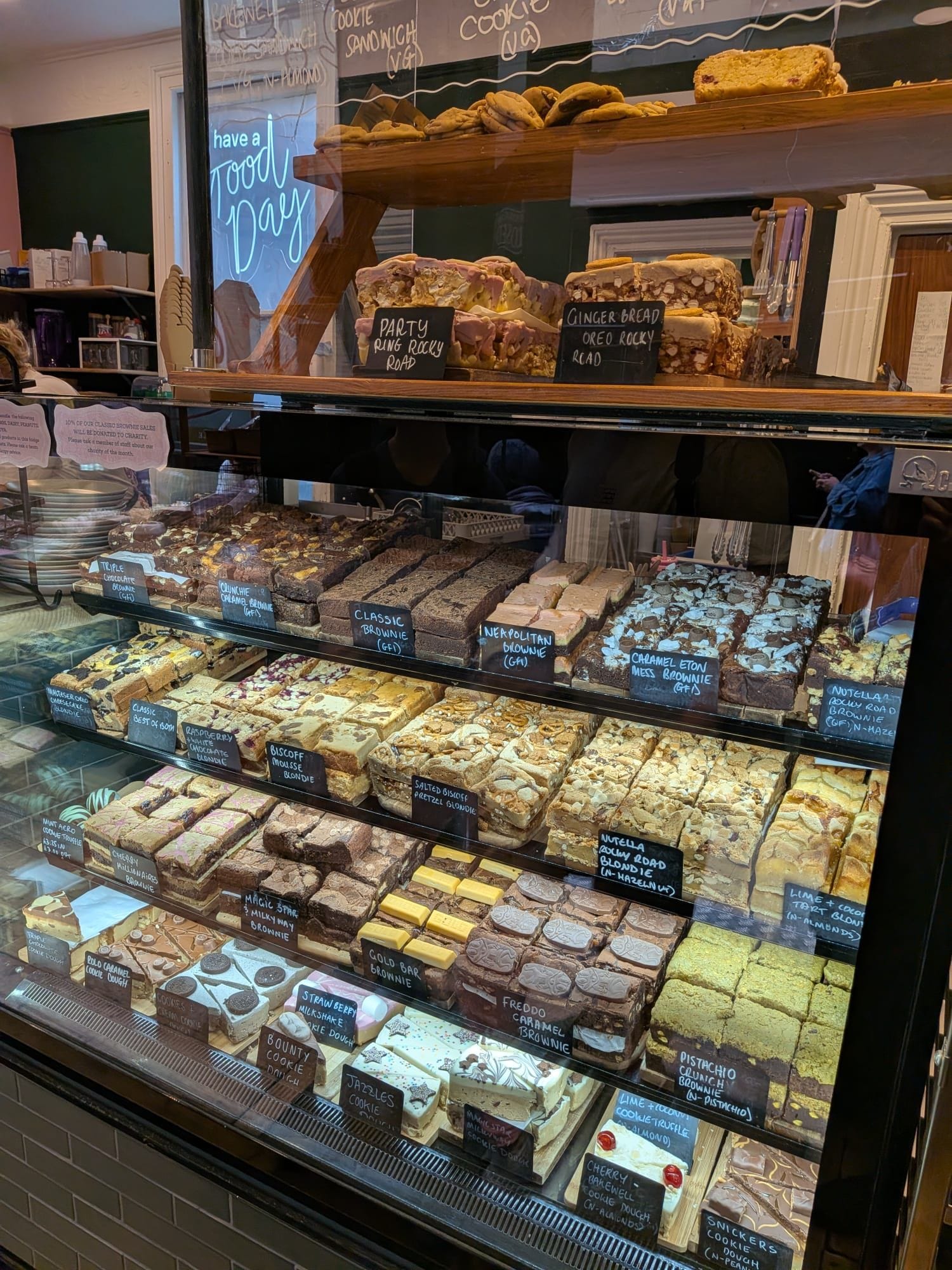 A display of amazing looking slices of brownies, blondies, cookie cakes, and more. They are all behind a glass screen. The counter is slightly visible to the left.