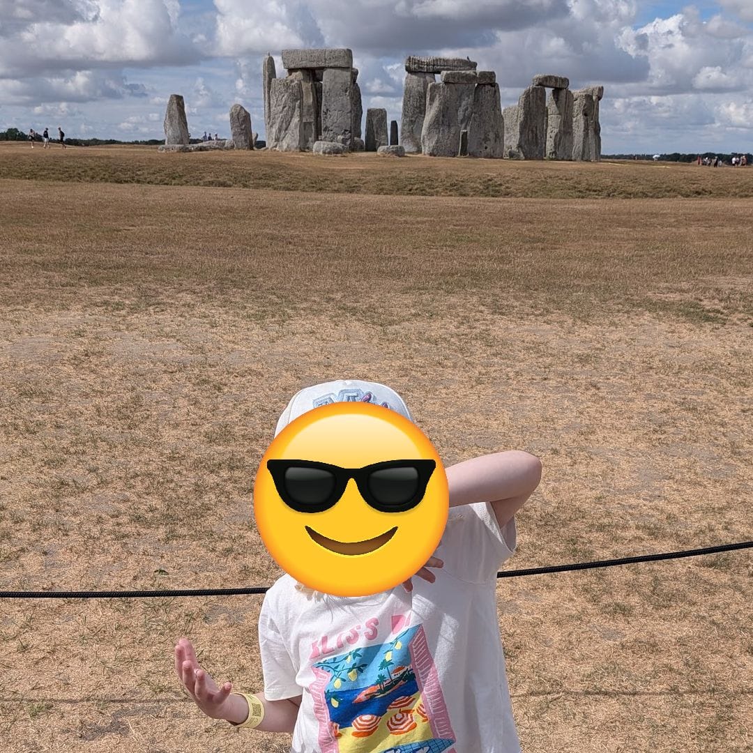 Stonehenge in the background as a small child poses, a yellow emoji face over her real face.