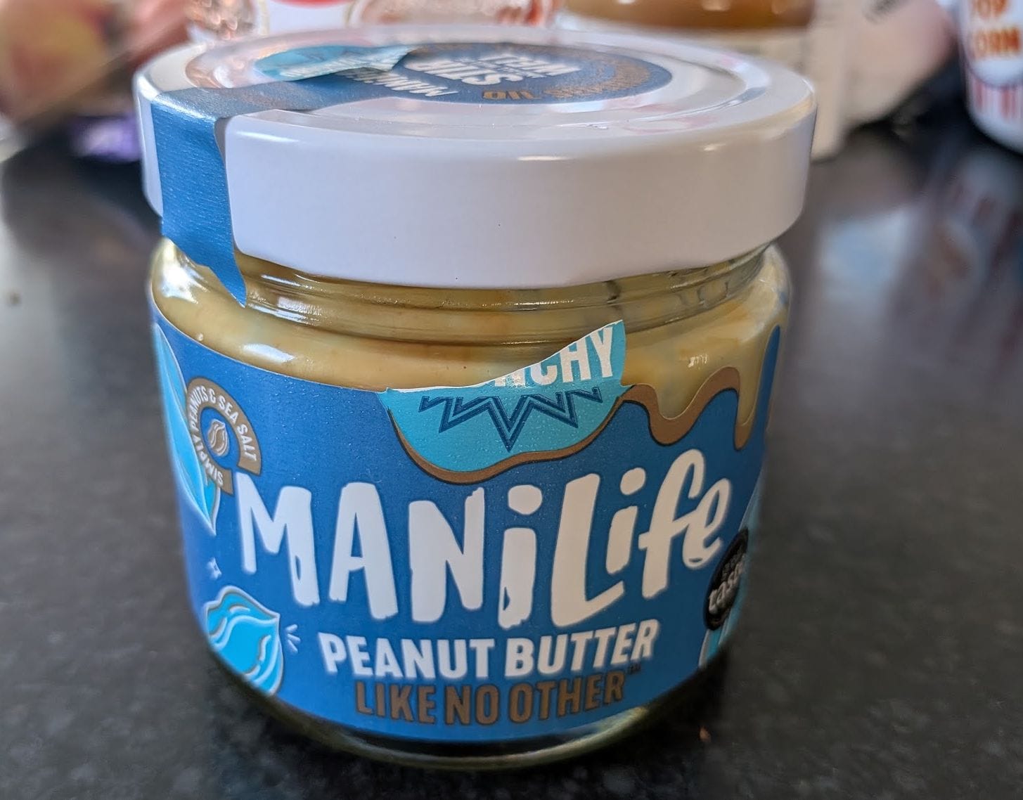 An opened and used jar of Manilife peanut butter, with a blue wrapper and white lid.