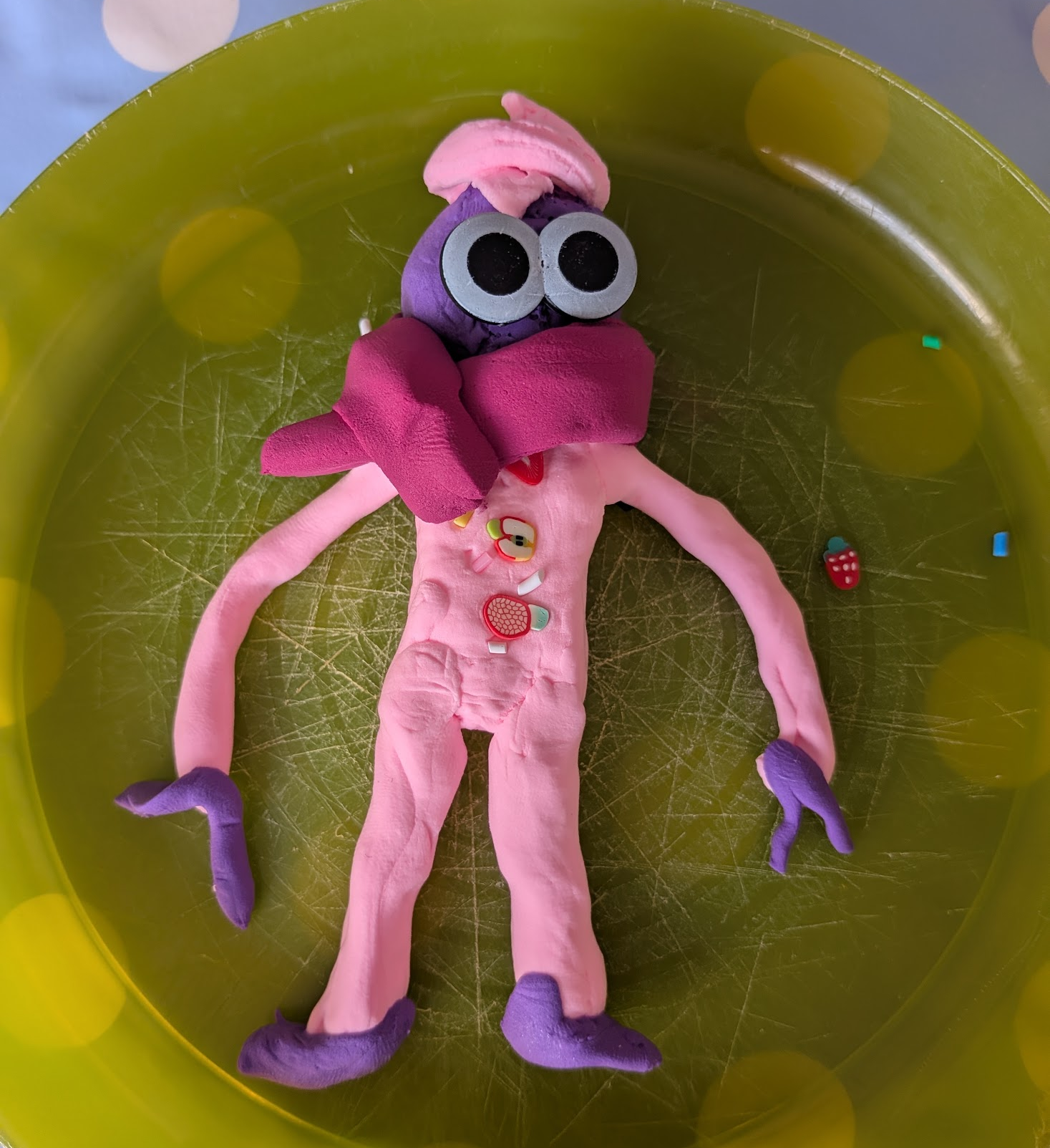 A purple man is dressed in a pink suit. He's got a pink hat and a reddish pink scarf. He's the coolest. Made from air dry clay.