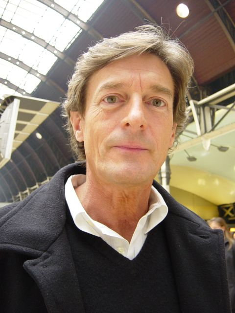 A photo of a man known to be Nigel Havers. He has swooshed hair and is wearing a shirt and jcoat.