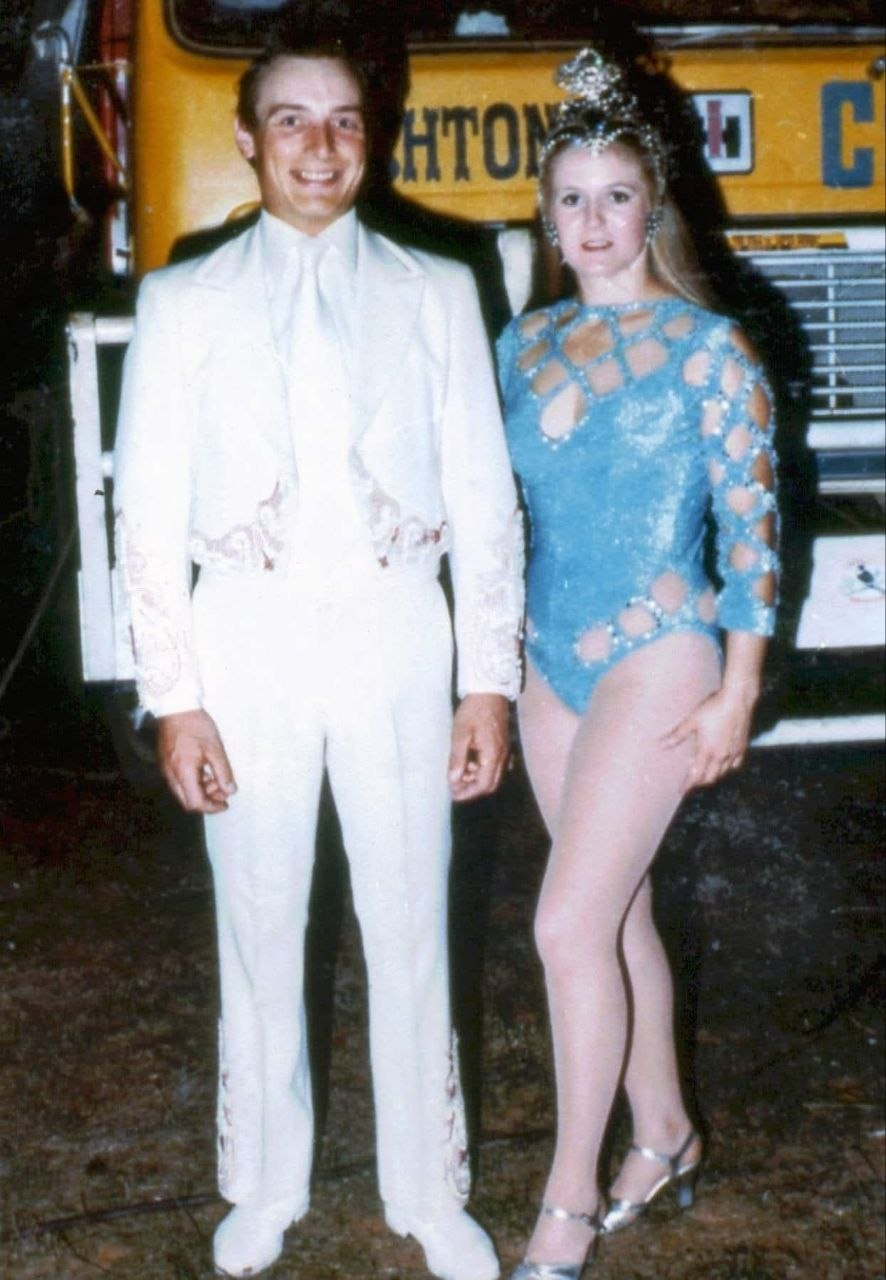 A photo of two circus performers wearing costumes, on front of an Ashton's Circus truck.