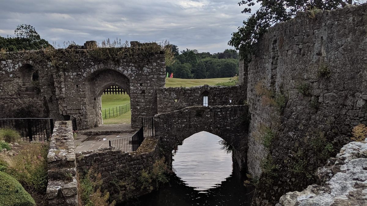 The castle grounds at Leeds Castle, with a small bridge over water. Green field in the background.
