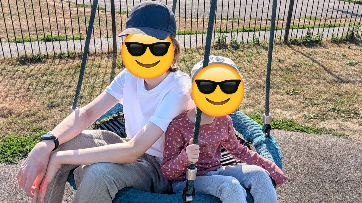 Two children, one older than the other, sat on a large swing, each with an emoji wearing sunglasses as a face.