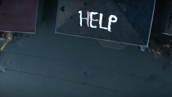 The word help is written out in clothes on the top of a house that is surrounded by flood water.