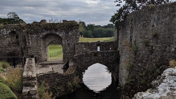 The castle grounds at Leeds Castle, with a small bridge over water. Green field in the background.
