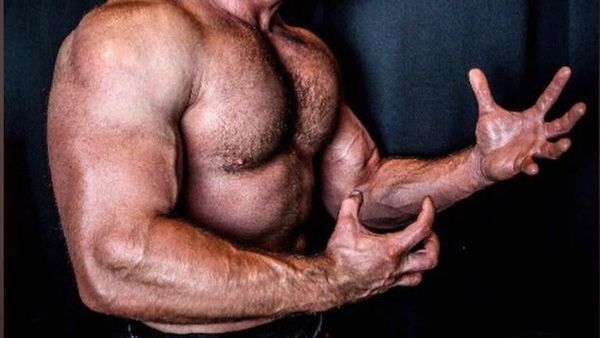 A close up photo of a man with huge arms and muscles, doing a kind of flex.